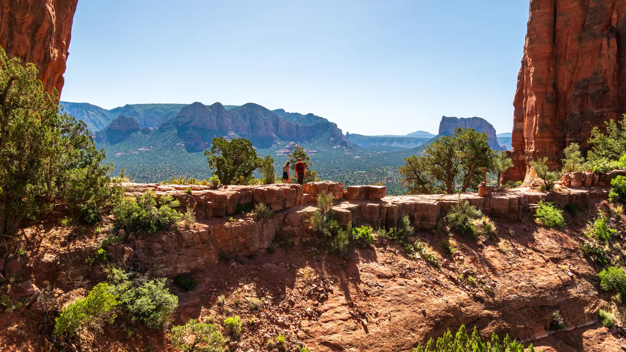 Red cliffs of Cathedral Rock framing a green valley and distant mesas in Sedona red rock country, Coconino National Forest