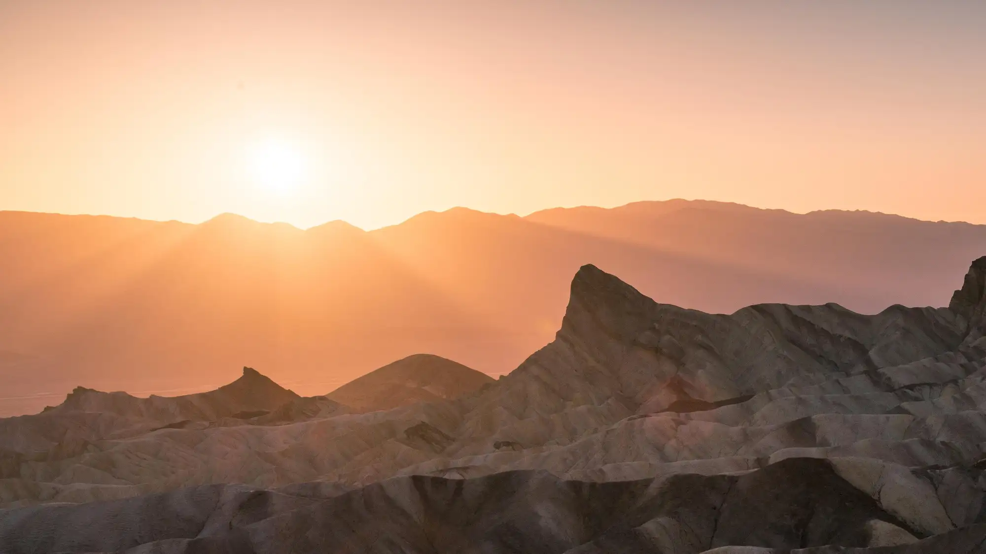 badlands bathed in pale pink and orange light from the setting sun