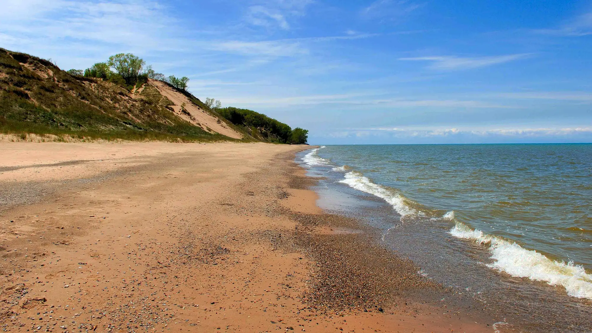 Michigan Lake beach with green grassy dunes in the background, under a blue sky.