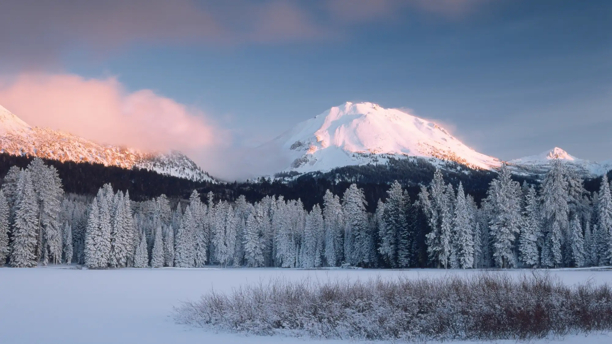 A frozen lake below snow-covered trees and peak