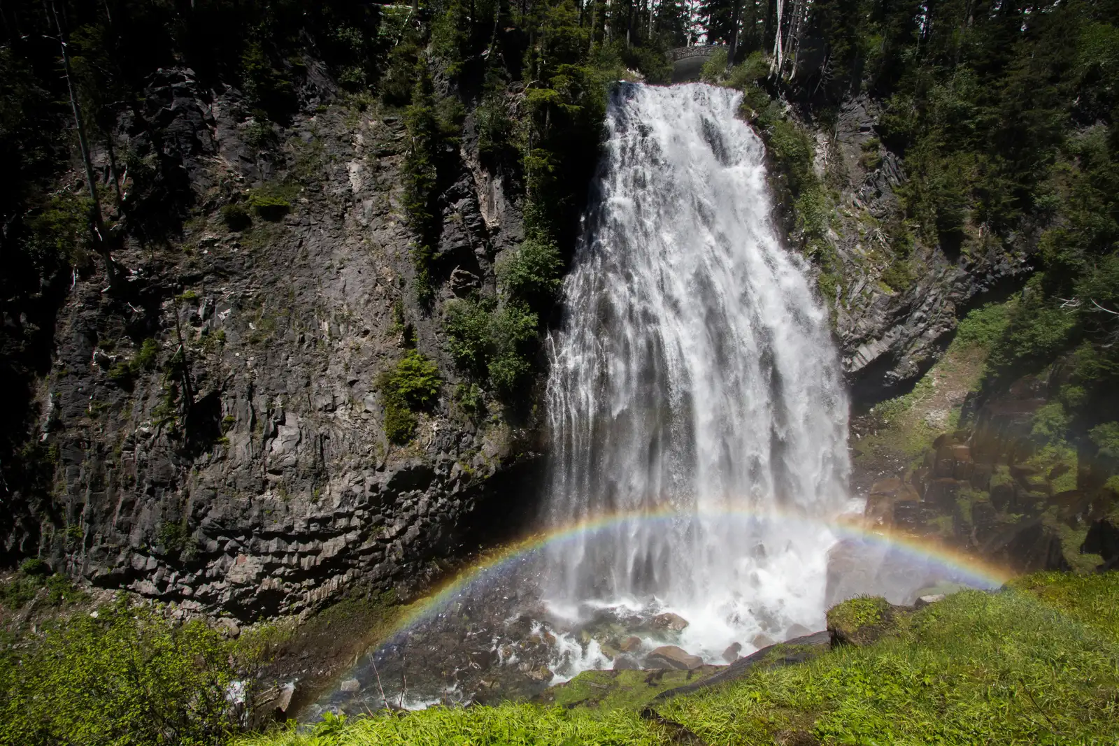 A fan-shaped waterfall cascades over lava cliffs with a rainbow in its mist.