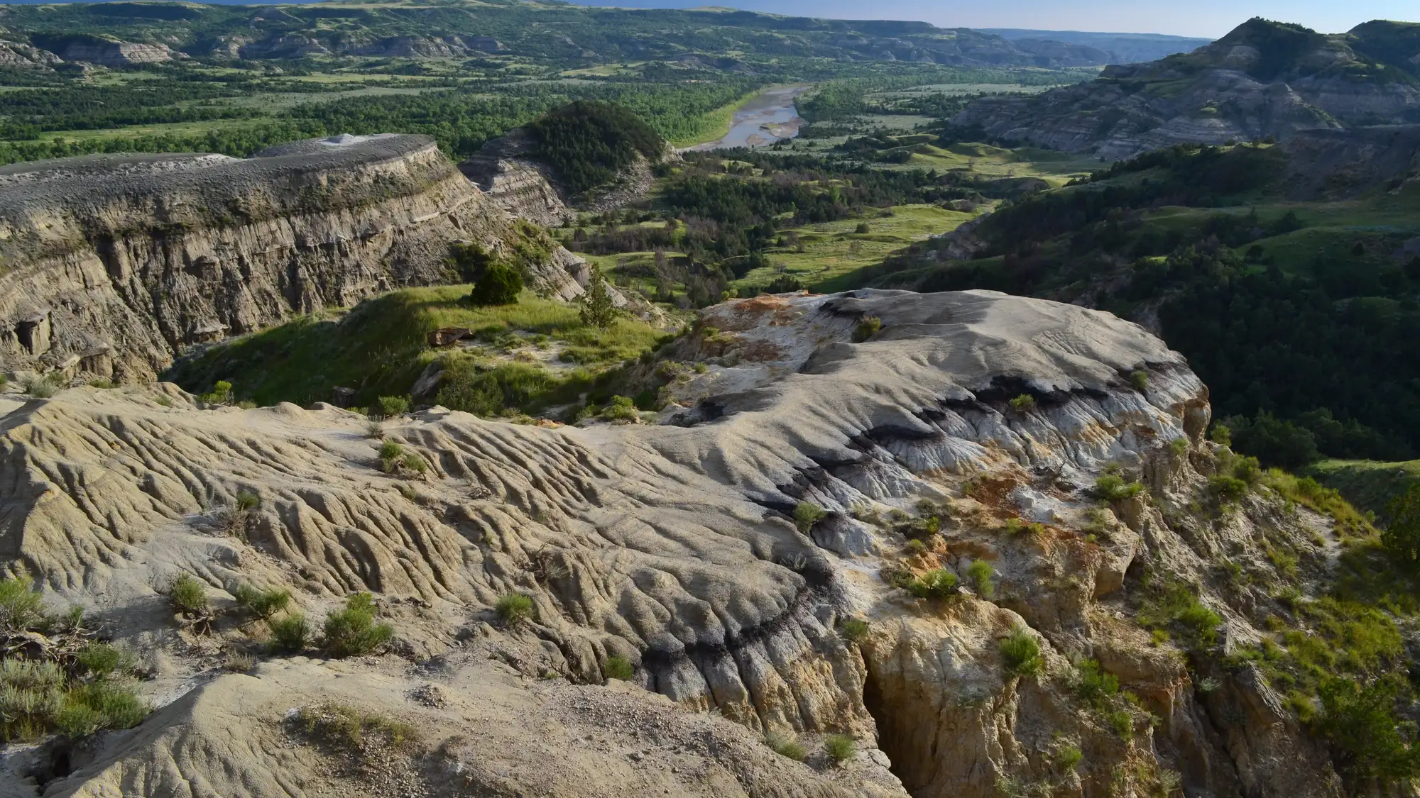 A colorfully striped butte in the foreground overlooks a dark green badlands landscape