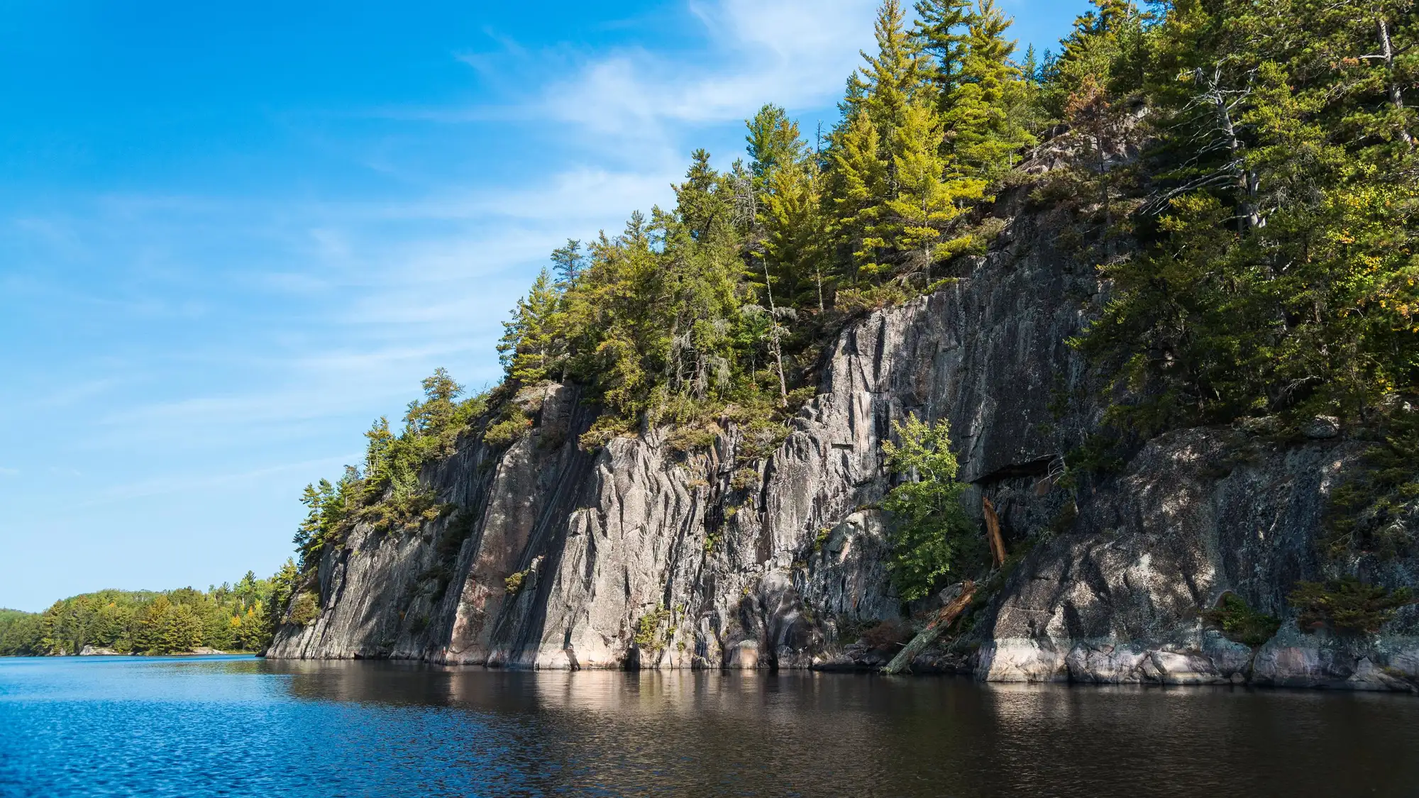 Photograph of granite cliffs topped with trees alongside a blue lake.