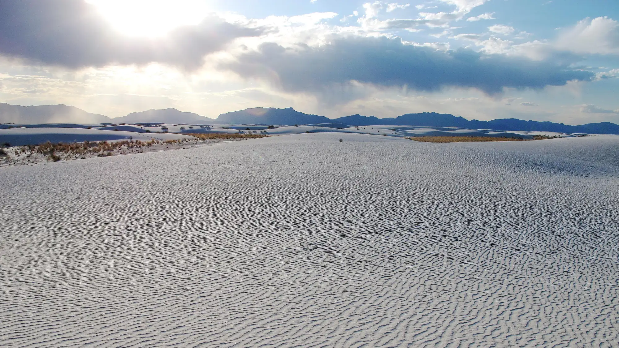 White dunes in foreground with sun setting behind mountain.