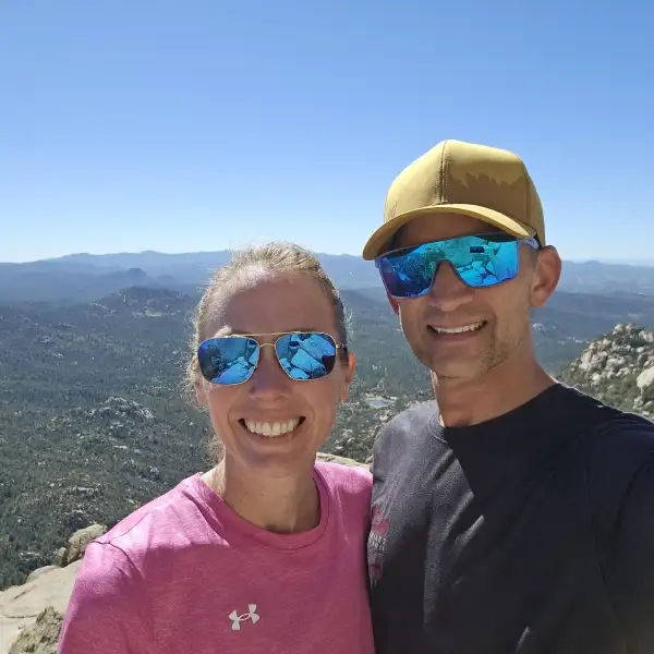 Ashley and Andrew smiling together at a mountain summit with forested ridges behind them